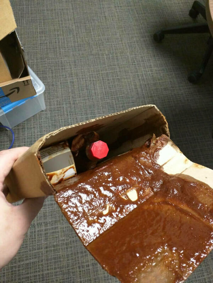 A hand holds a cardboard package spilling a thick brown liquid, a clear example of delivery fails.
