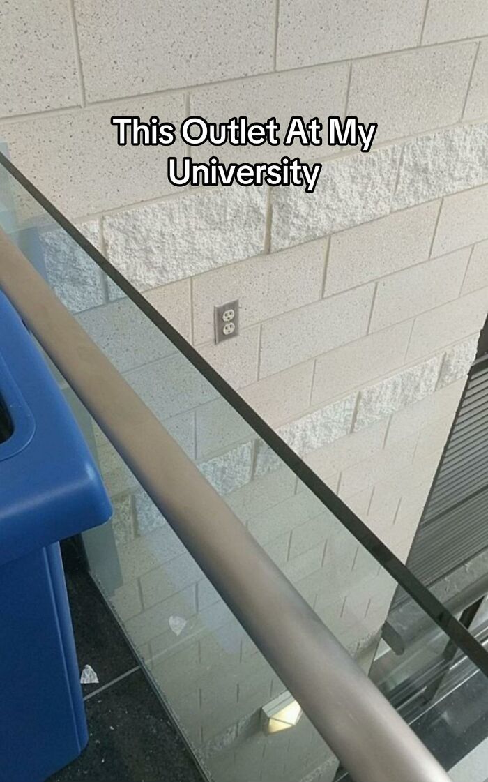 A hilariously bad design fail: an electrical outlet is placed high on a wall, behind a glass and metal railing, making it unusable.