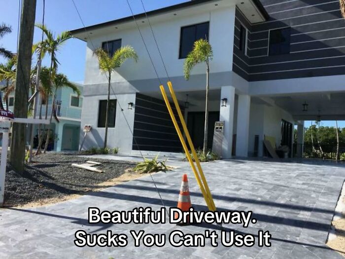 A newly built house with a blocked driveway due to two yellow poles and a traffic cone, a bad design fail.