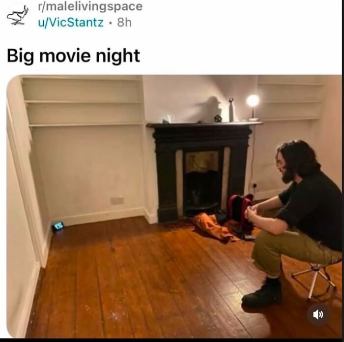 A man with long hair sits on a stool in an empty room, creating a funny scene for a big movie night.