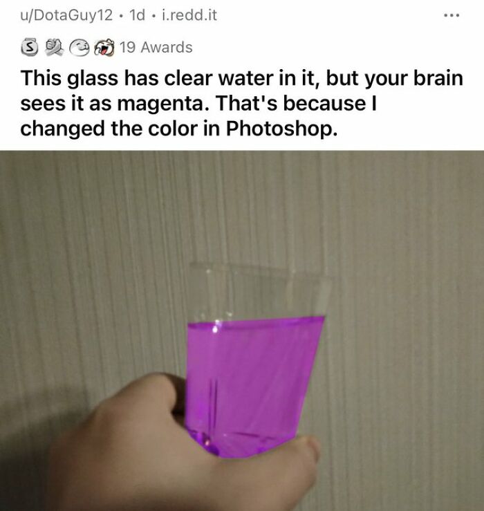 A hand holding a clear glass of water that appears magenta due to a funny Photoshop trick.