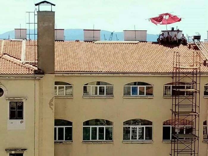 People on a tiled rooftop with a red umbrella, next to a tall chimney, an example of Slavic Science.