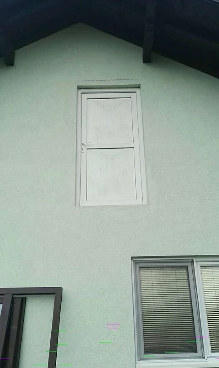 An exterior wall of a house featuring a door placed high up with no balcony, an example of Slavic Science.