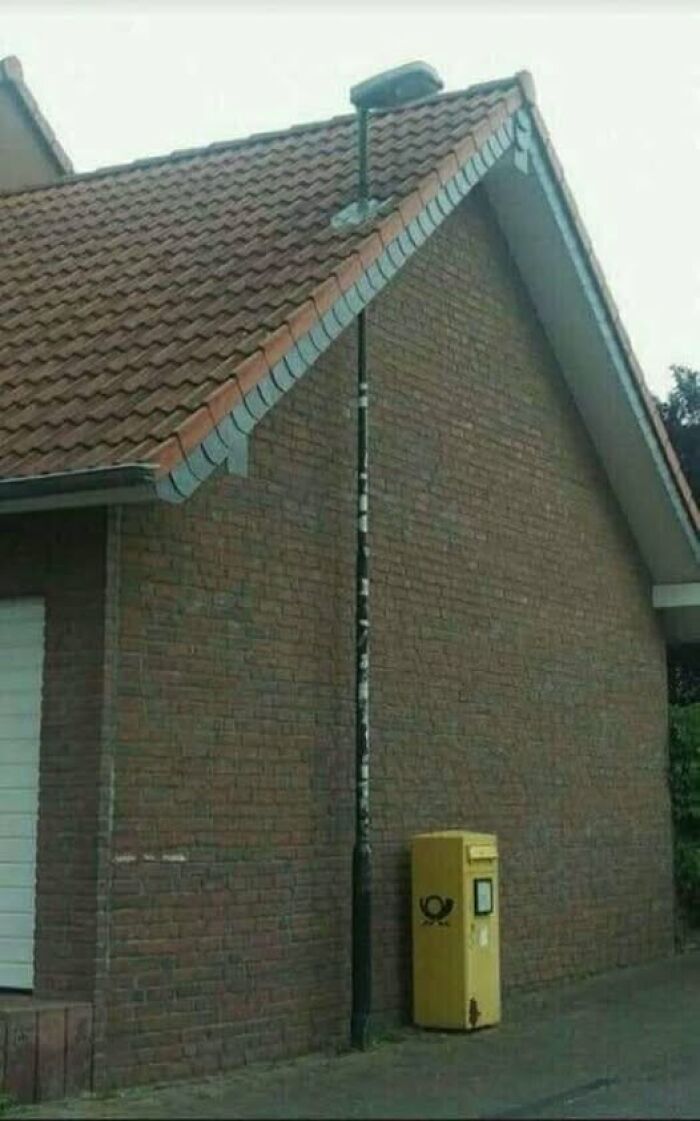 A lamppost integrated into a brick house wall next to a yellow mailbox, showing unusual Slavic science.