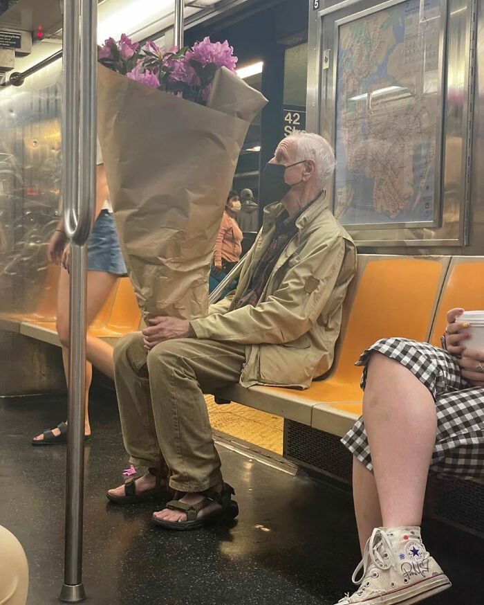 An elderly man wearing a mask and sandals sits on a subway with a huge bouquet of flowers, a legendary internet photo.