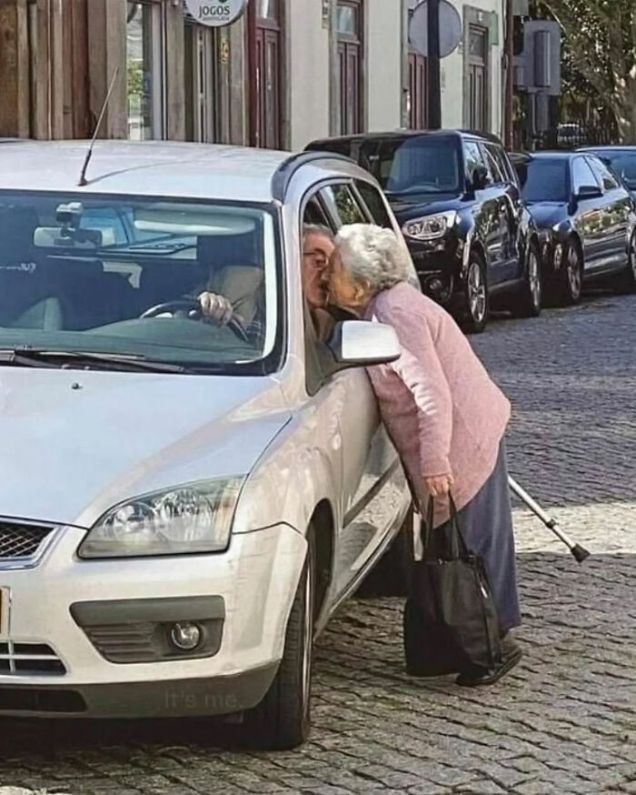 An older woman leans into a car window to kiss a man, a heartwarming photo that became a legend.