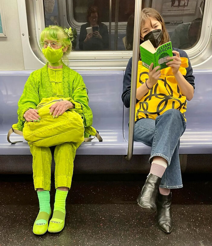 A woman in a full green outfit and mask sits on a subway, a great photo that became a legend.