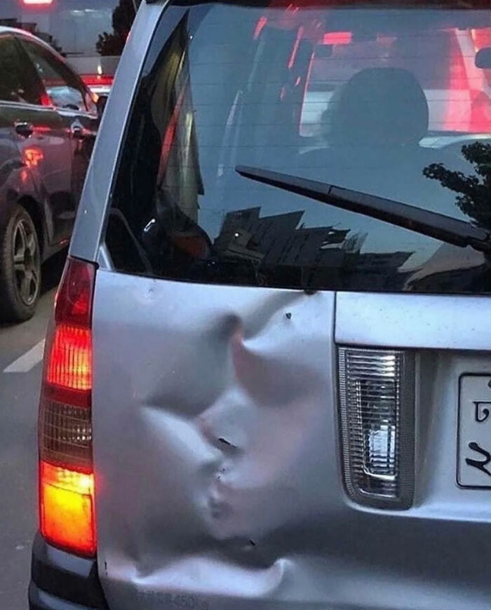 The dented rear bumper of a silver car forming a face, captured in one of the great photos.