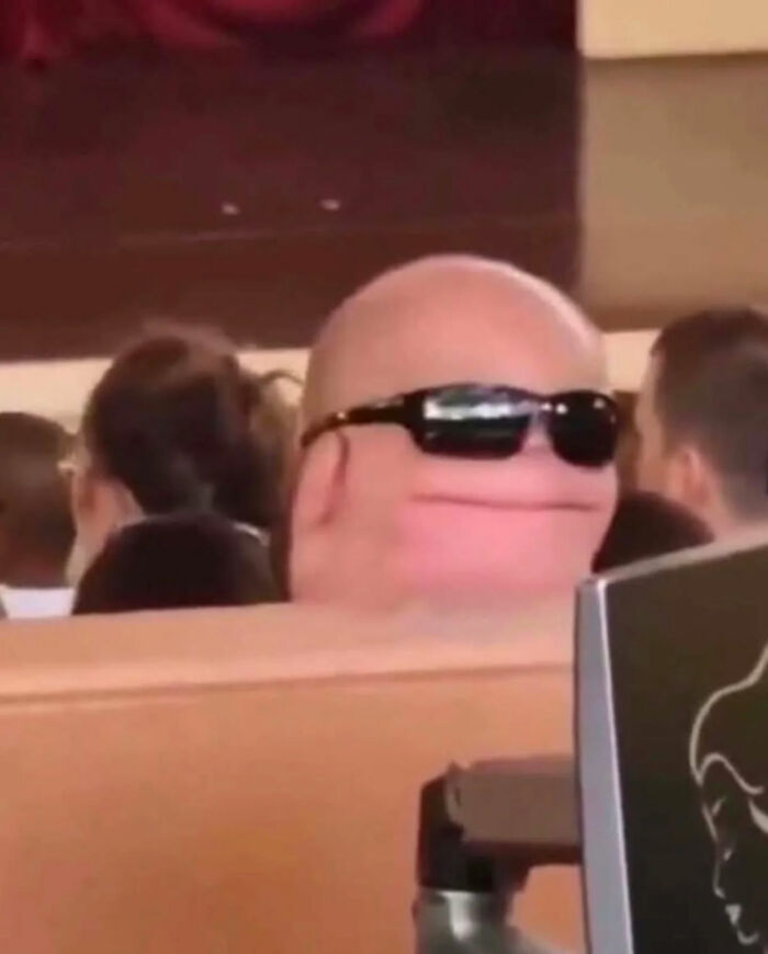 A bald person with large sunglasses and a wide smile, a funny photo and internet legend.