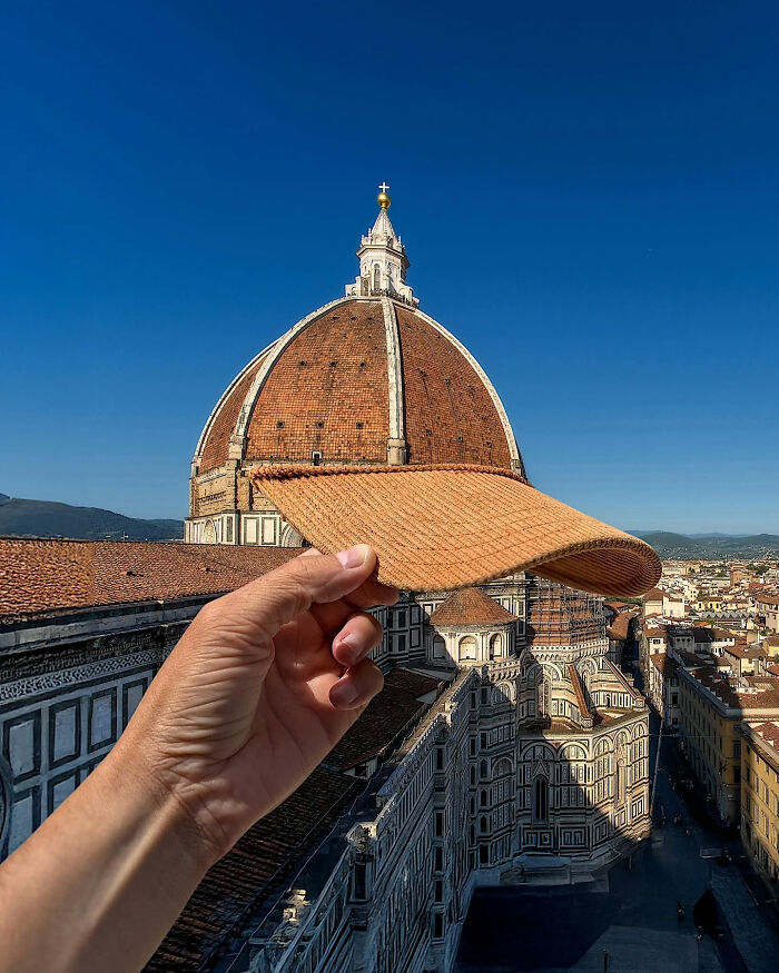 A hand holding up a straw hat brim perfectly aligned to look like the dome of a building, a great internet legend.