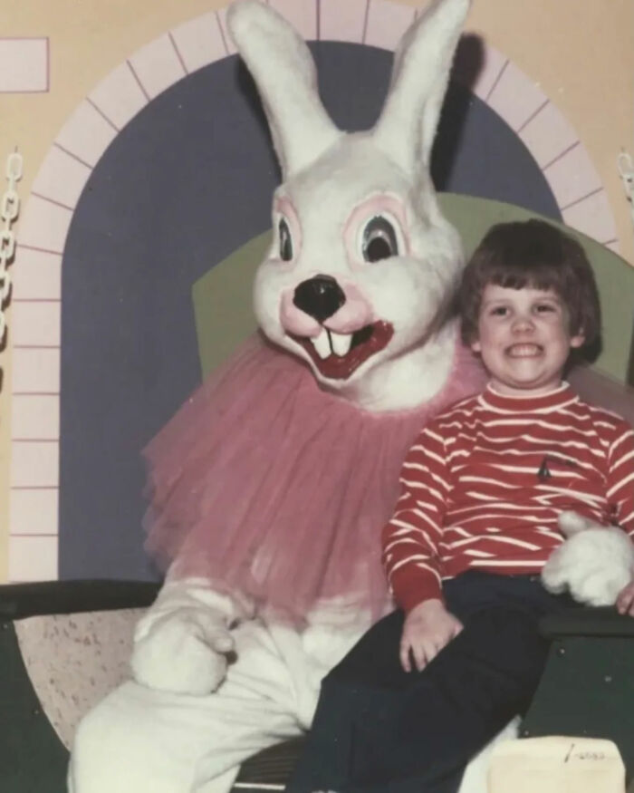 A young child in a striped shirt smiling while sitting next to a somewhat creepy Easter Bunny, a legend of the internet.