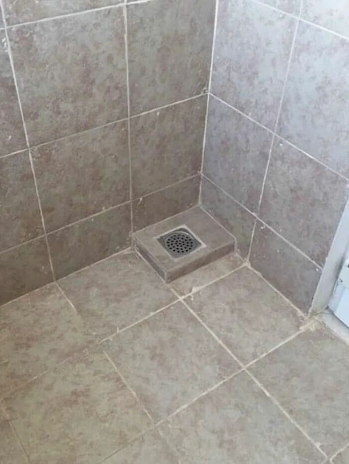 An oddly placed shower drain on a raised tile platform in a shower, one of the internet legends.