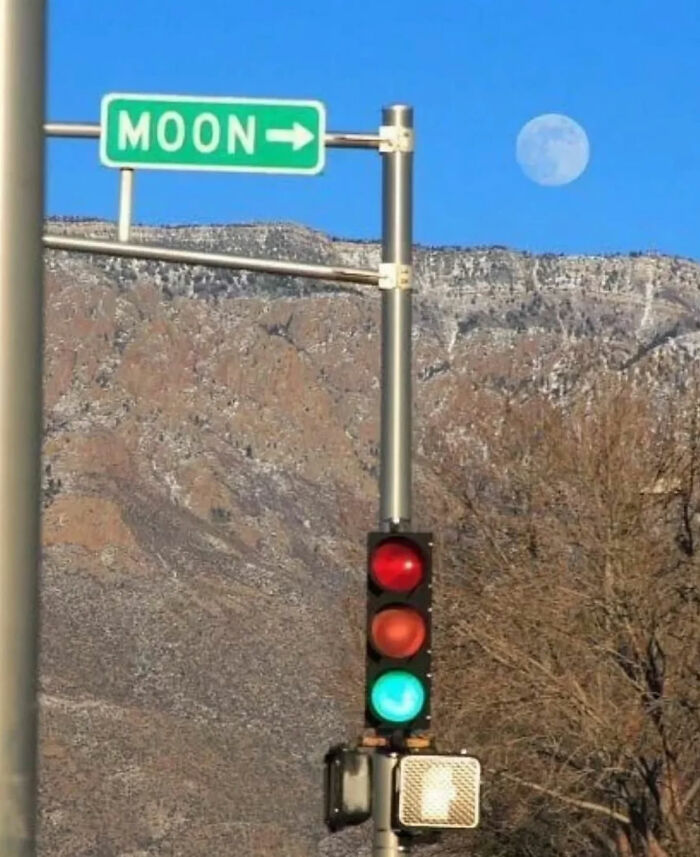 A Moon street sign pointing towards the moon in the sky above mountains, one of the internet's great photos.