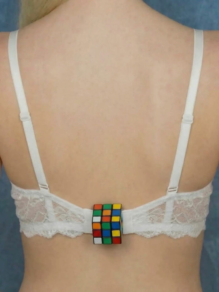 The back of a woman wearing a white lace bra with a solved Rubik's Cube attached to the clasp, a great photo.