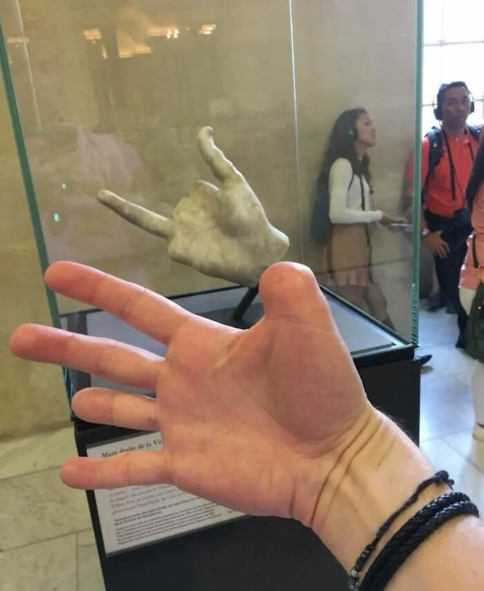 A hand mimicking a rock and roll sign next to a historic sculpture of a hand making a similar gesture, a legend of the Internet.