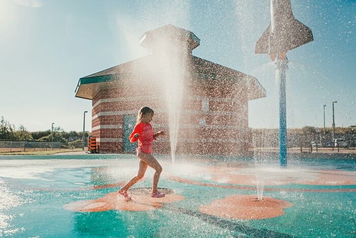 A small girl running through water at a splash pad. She is not a teacher or entitled parent.