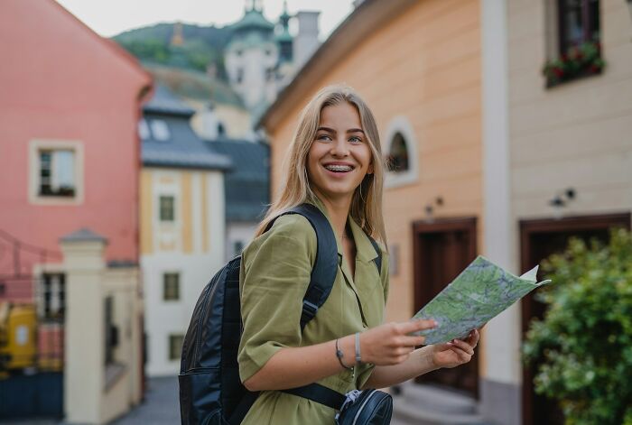Smiling tourist with backpack holding a city map on a street with historic buildings