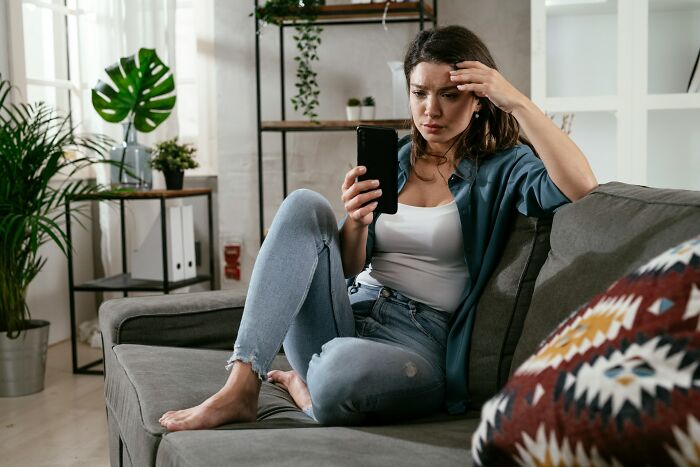 Upset woman sitting on sofa discovering shocking things on phone