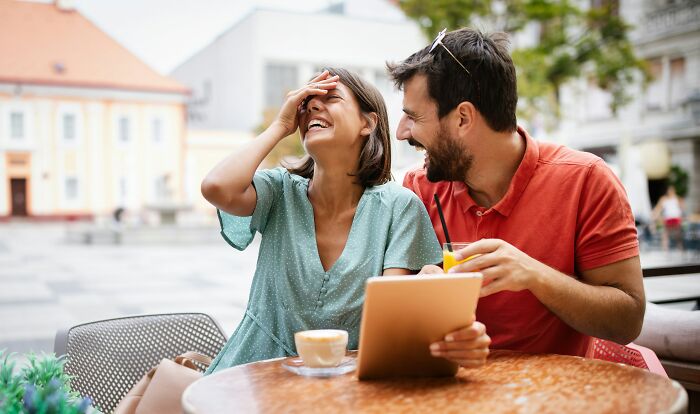 Happy couple laughing together at an outdoor cafe, a moment women decide to marry their partner.