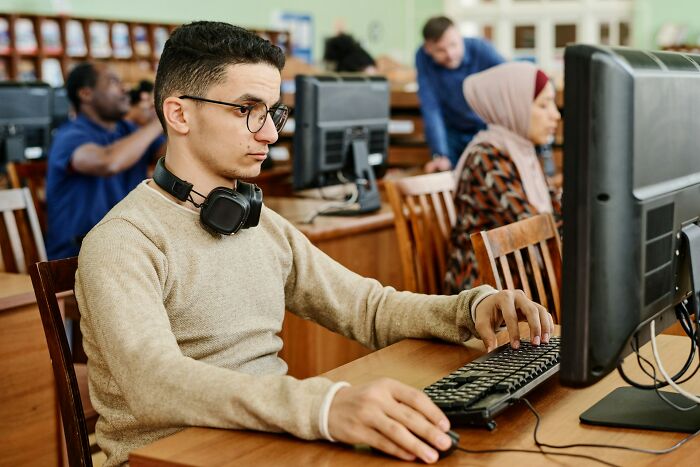 Young man with headphones on, working intently at a computer, potentially leading to intense stress and burnout.