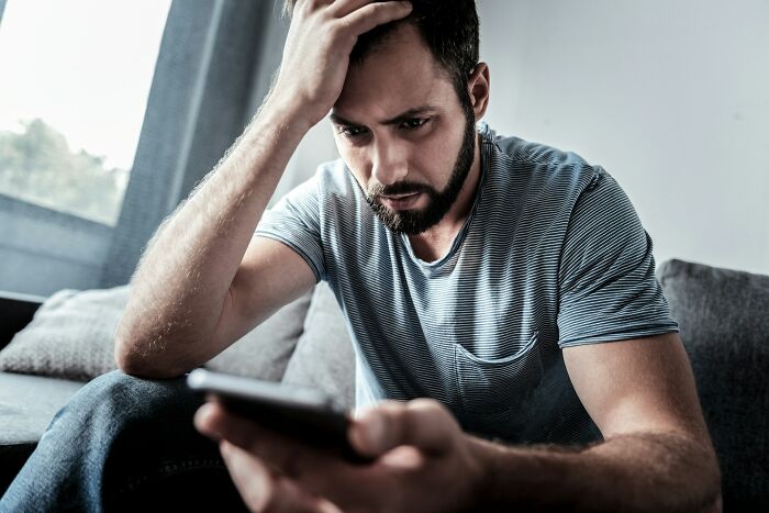 A man looking worried while holding his phone, feeling the bed compress due to unexplained experiences.