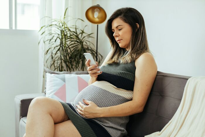 Pregnant woman looking at phone while resting on couch with baby bump