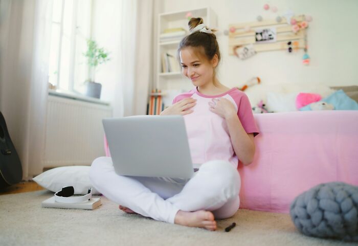 Smiling young woman sitting on floor with laptop in cozy bedroom