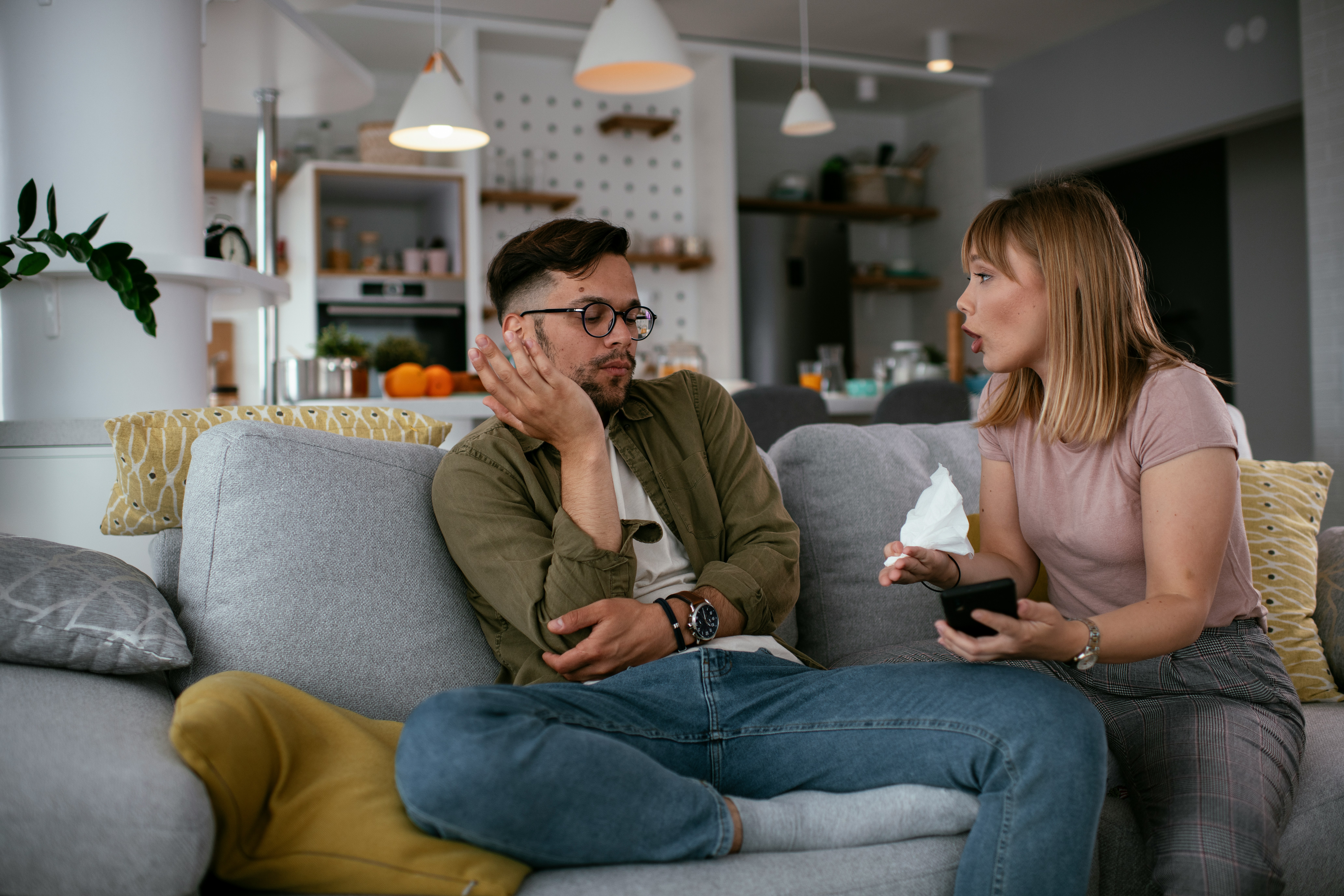 Husband looking frustrated as wife talks, holding tissues, about the dreaded annual family trip with in-laws.