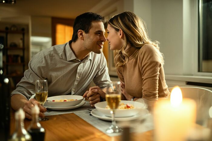 A couple leaning in for a kiss during a candlelit dinner, revealing surprising double lives.
