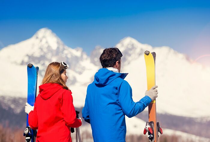 Couple holding skis in winter mountains enjoying satisfying relaxation after betrayal