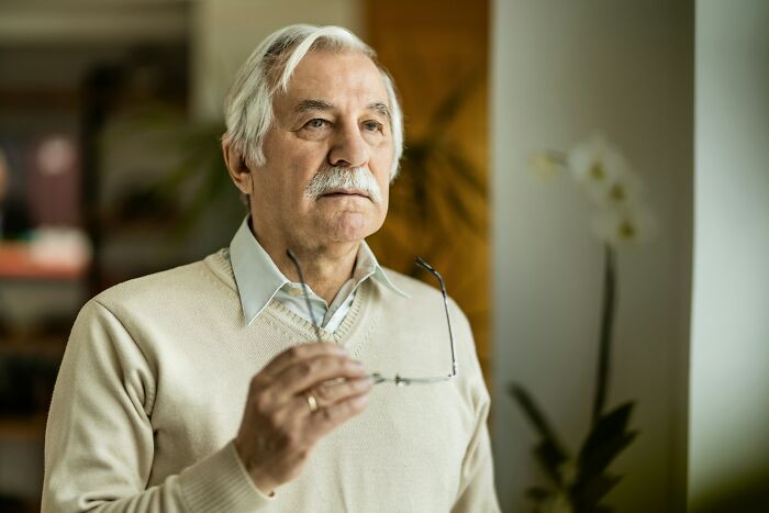 Elderly man holding glasses reflecting on Gen Alpha literacy challenges