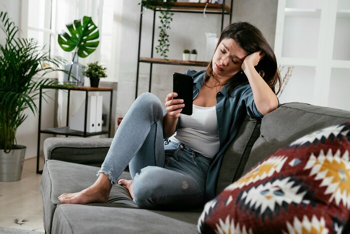 Woman upset on couch holding phone in cheating and complete idiots story