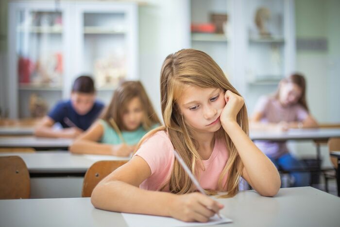 Bored schoolgirl looking frustrated while sitting at desk in classroom