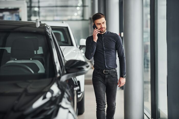 A man talking on a phone in a car showroom, highlighting various unusual jobs people somehow managed to get hired for.