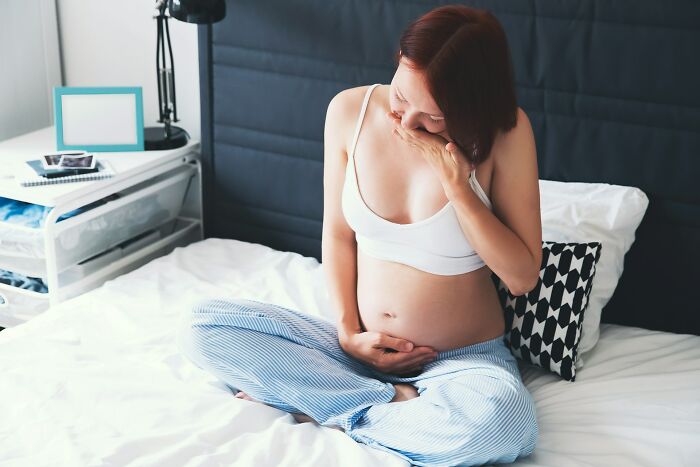 Pregnant woman feeling nauseous holding belly in bedroom, human body fact theme