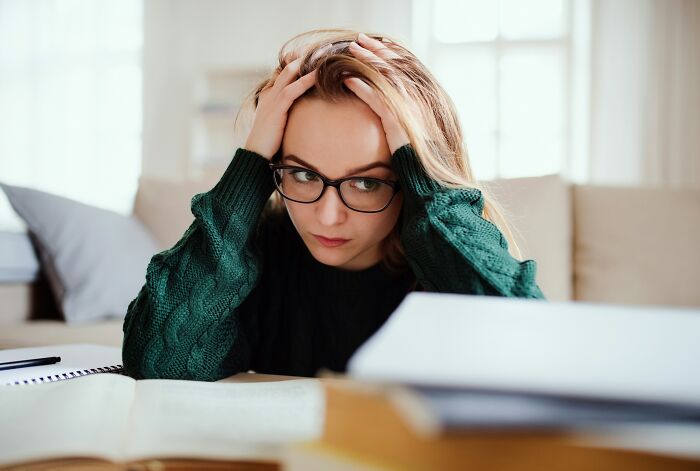 A worried woman teacher with hands on her head, looking at a message from entitled parents.