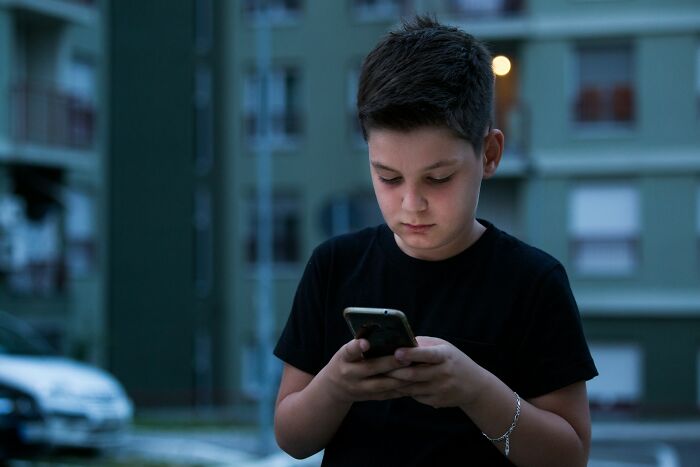 Gen Alpha boy focused on smartphone outdoors at dusk