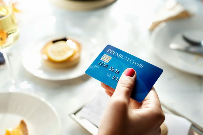 A hand with red nail polish holding a blue premium credit card, a payment method for things while visiting the US.