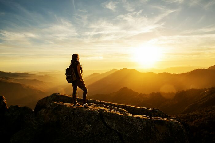 A woman on a mountain top enjoying the sunset, representing finding strange jobs and earning money unconventionally.
