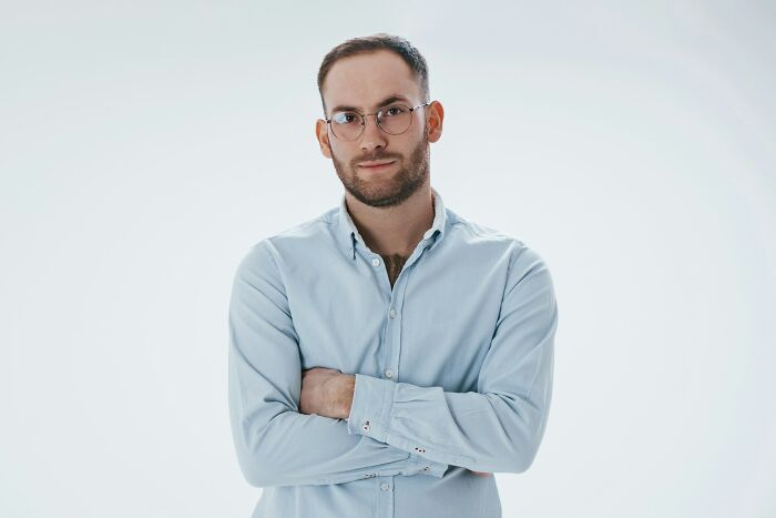 A secretly smart man in glasses with arms crossed, looking intently, showing hints of intelligence.