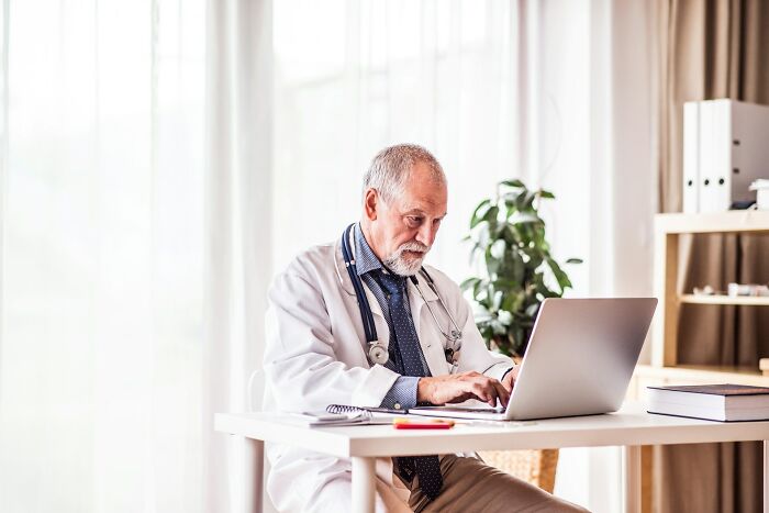A male doctor in a white coat working on a laptop, representing doctors managing intense stress and burnout.