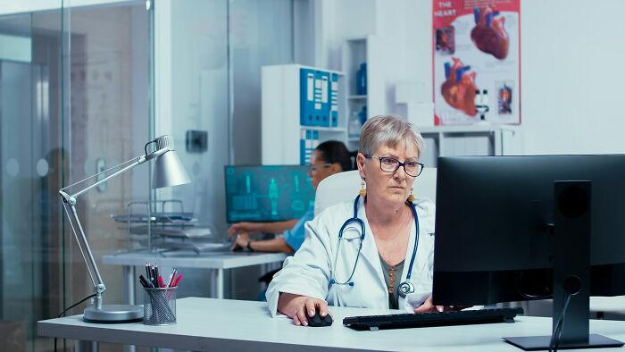 A female doctor works at a computer in a clinic, managing health trends and patient care to prevent intense stress and burnout.