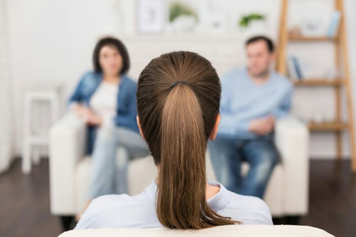 A therapist facing away, with a divorced couple blurred in the background, discussing their marriage that was over.