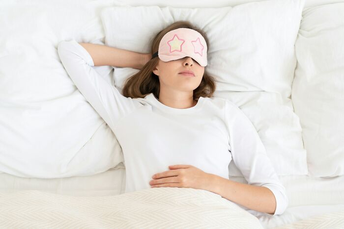 A woman sleeping in bed with a pink eye mask, highlighting strange jobs and unconventional ways to earn money.