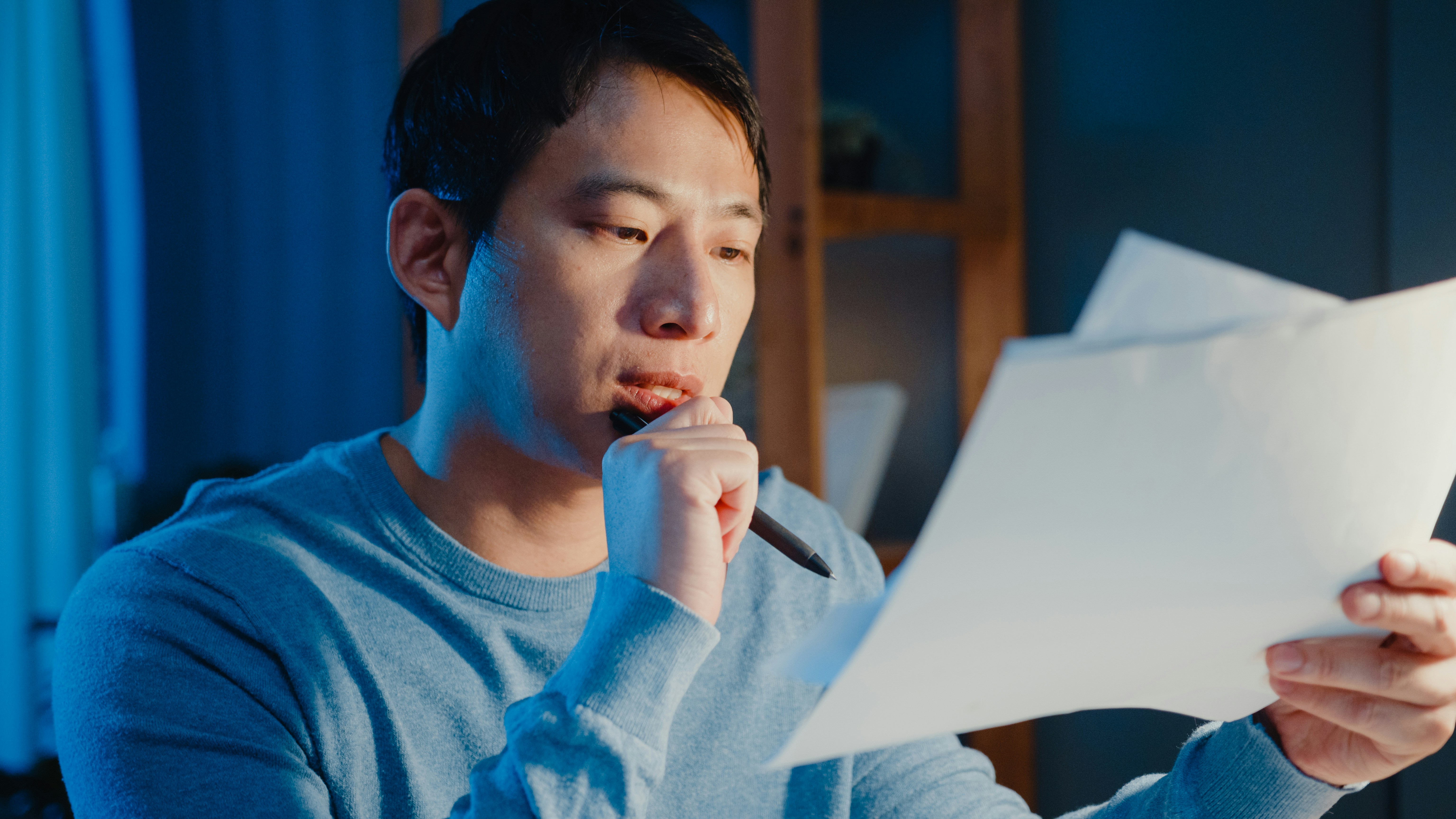 A man with a pensive expression, holding papers and a pen, discovers his husband living a double life.