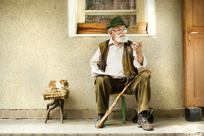 Elderly man with cane sitting outside with cat pondering family secrets
