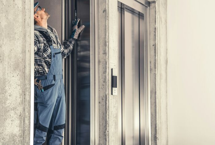 A repairman in overalls working on an elevator, an example of strange jobs for earning money.