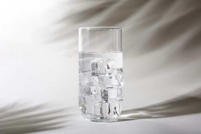 Glass filled with water and ice cubes on white surface