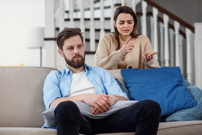 Couple sitting on couch, woman upset, man avoiding conversation
