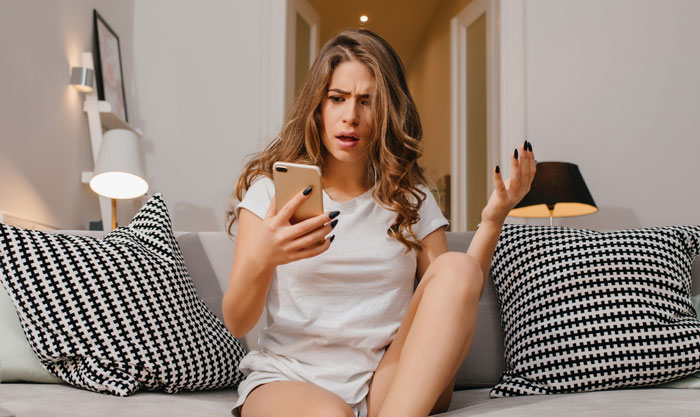 Woman looking shocked at phone showing emotional reaction to explicit photos